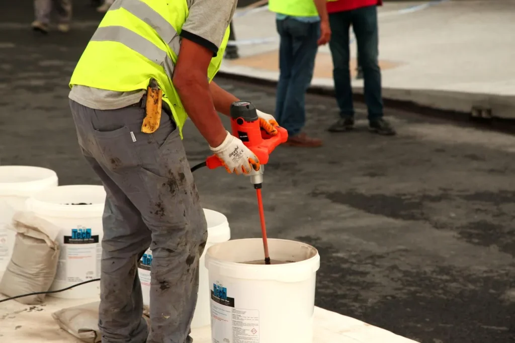 Worker using a mud mixer to blend mortar with construction chemical additives
