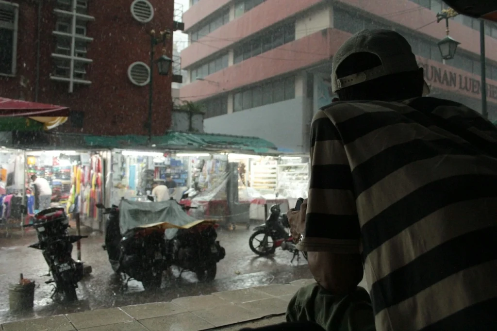 Man sheltering from torrential monsoon rain on a Kuala Lumpur street, highlighting the wet conditions buildings face in Malaysia